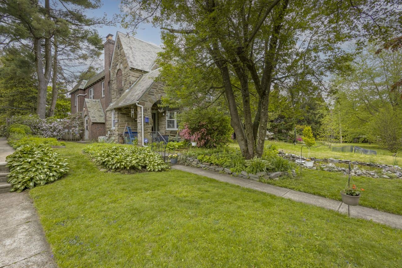 Charming stone house with lush garden and mature trees in a peaceful neighborhood.